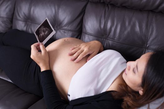 Pregnant woman resting on sofa and holding her child ultrasound picture