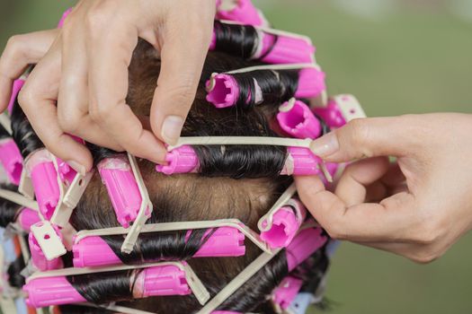 hand of a hairstylist doing a perm rolling the hair of senior woman