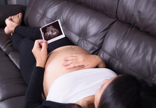 Pregnant woman resting on sofa and holding her child ultrasound picture