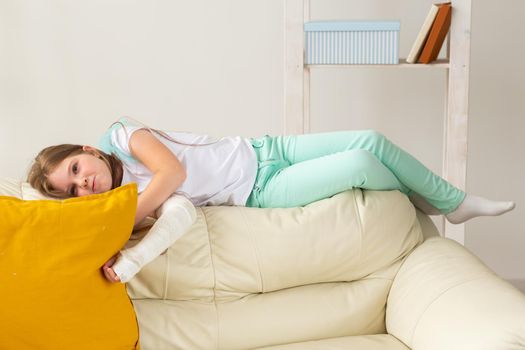 Child with a cast on a broken wrist or arm smiling and having fun on a couch. Positive attitude, recovery and kid.