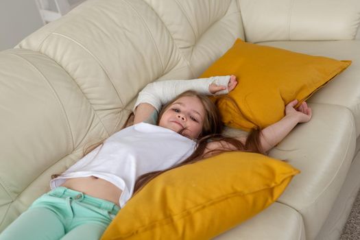 Child with a cast on a broken wrist or arm smiling and having fun on a couch. Positive attitude, recovery and kid.