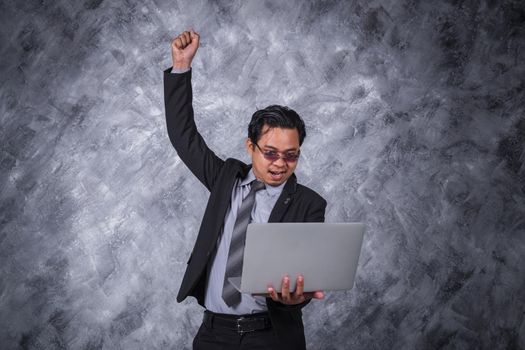 young winner business man holding laptop with arms raised 
