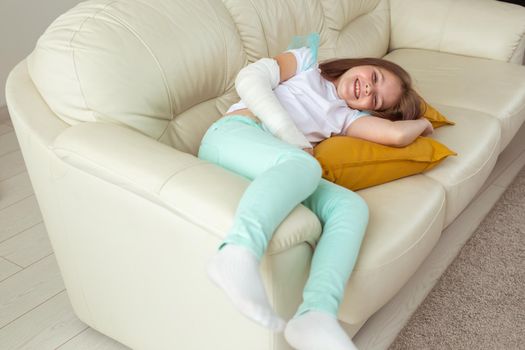 Child with a cast on a broken wrist or arm smiling and having fun on a couch. Positive attitude, recovery and kid.