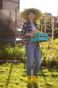 Positive young woman gardener holds box of lemons in her hands during the harvest at her firm.