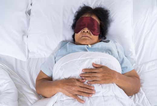 senior woman with eye mask sleeping on a bed in bedroom