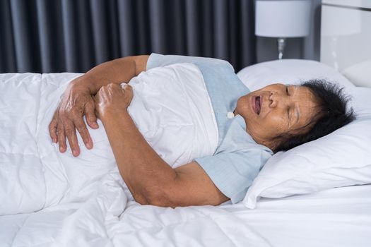 senior woman suffering from stomachache on bed at home