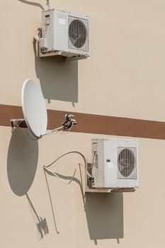 Air conditioners and satellite dish on the wall of a modern house on the street outdoor.