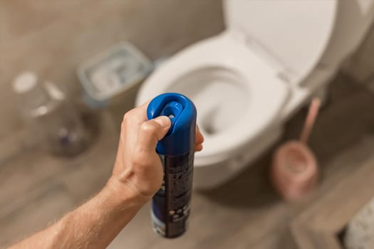 The guy's hand holds and sprays the air freshener in the toilet or bathroom. Home Hygiene Concept.