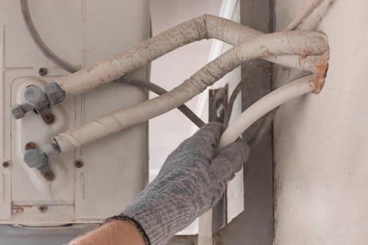 The hand of an air conditioner repair and maintenance specialist in a construction glove working with air-conditioned old equipment.