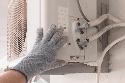 The hand of an air conditioner repair and maintenance specialist in a construction glove working with air-conditioned old equipment.