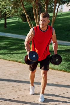 athletic man with dumbbells in his hands outdoors in the park. High quality photo