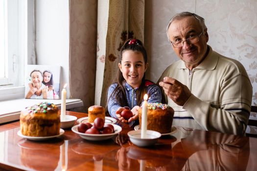 happy grandfather and granddaughter hold easter eggs in hand, folk game beats easter egg.