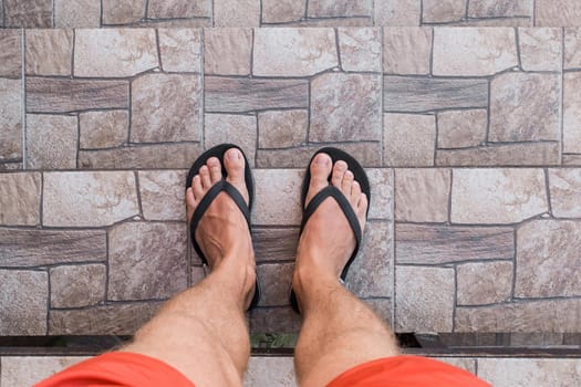 Men's legs in black flip flops and red shorts go down and walk down the stairs. Walking style.