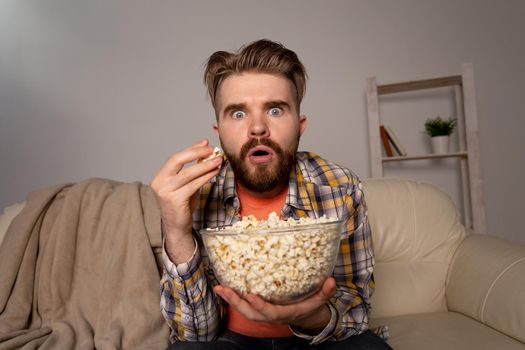 Bearded man watching film or sport games TV eating popcorn in house at night. Cinema, championship and fan.