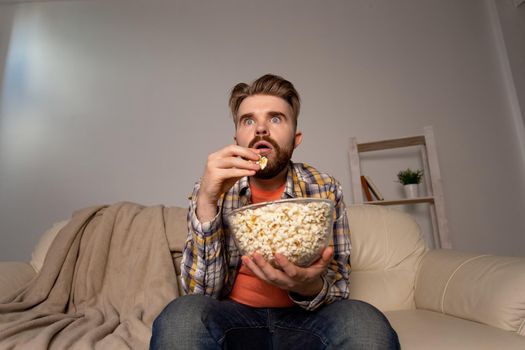 Bearded man watching film or sport games TV eating popcorn in house at night. Cinema, championship and fan.