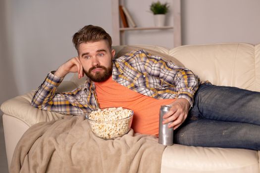 Bearded man watching film or sport games TV eating popcorn in house at night. Cinema, championship and fan.