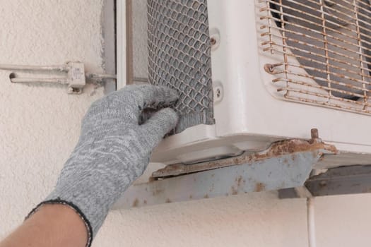 The hand of an air conditioner repair and maintenance specialist in a construction glove working with air-conditioned old equipment.