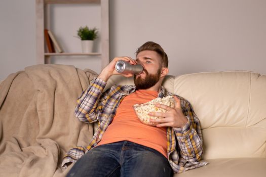 Bearded man watching film or sport games TV eating popcorn in house at night. Cinema, championship and fan.