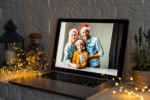Happy parents hugging cute small kid daughter holding present giving Christmas gift to web camera during virtual family social meeting on video conference call party at home, laptop webcam view