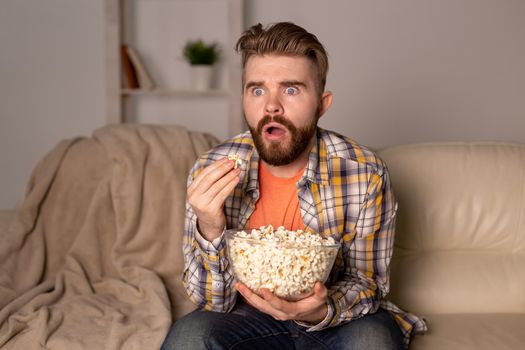 Bearded man watching film or sport games TV eating popcorn in house at night. Cinema, championship and fan.
