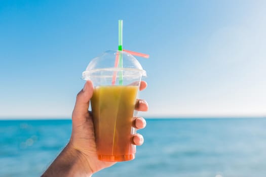 The guy's hand holds a colored chilled non-alcoholic cocktail against the background of the sea.