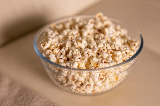 Bowl of popcorn for watching a film on a beige couch. Snacks and unhealthy junk food.