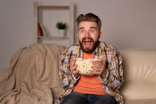 Bearded man watching film or sport games TV eating popcorn in house at night. Cinema, championship and fan.