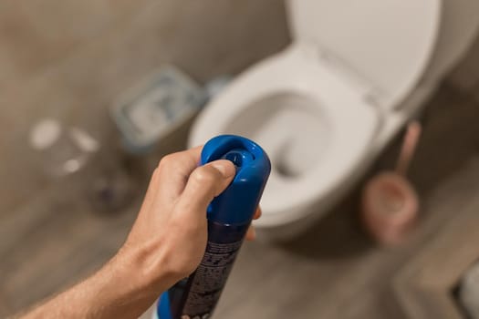 The guy's hand holds and sprays the air freshener in the toilet or bathroom. Home Hygiene Concept.