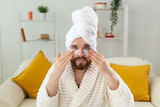 Young man with patches under the eyes at home. Concept of cosmetology for men.Spa at home, body and skin care.