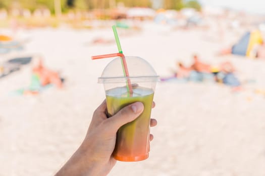 The guy's hand holds a colored chilled non-alcoholic cocktail against the background of the sea beach.