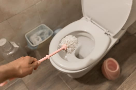 The guy's hand holds the toilet brush and cleans the toilet. The concept of home cleaning and hygiene in the bathroom.