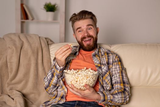 Bearded man watching film or sport games TV eating popcorn in house at night. Cinema, championship and fan.