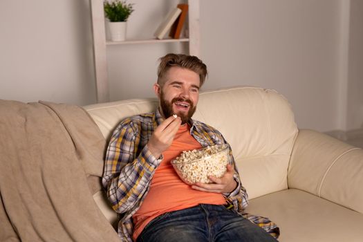 Bearded man watching film or sport games TV eating popcorn in house at night. Cinema, championship and fan.