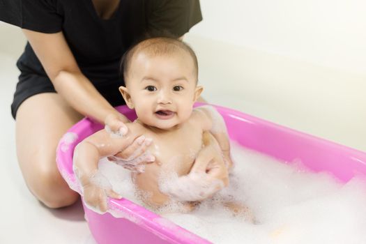 baby taking a bath in bathtub and playing with foam bubbles at home