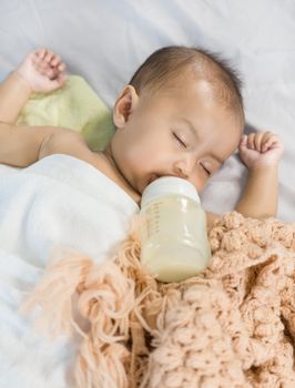 baby drinking milk from bottle and sleeping on bed at home