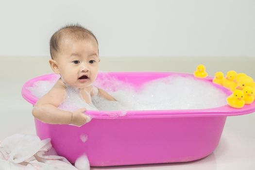 baby taking a bath in bathtub and playing with foam bubbles at home