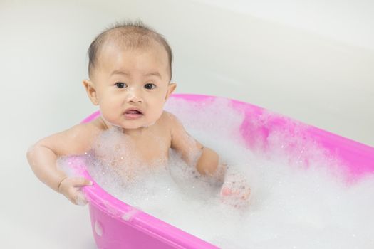 baby taking a bath in bathtub and playing with foam bubbles at home