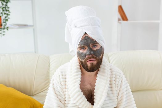 Bearded man has clean fresh skin, wears beauty clay mask on face and enjoys beauty treatments. Spa at home, body and skin care.