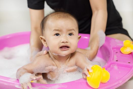 baby taking a bath in bathtub and playing with foam bubbles at home