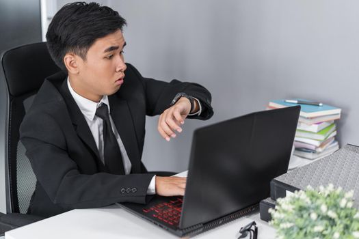 young business man checking time on watch while using laptop