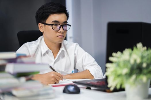 young man studying and writing on notebook with laptop computer