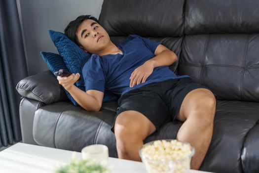 young bored man watching tv and sitting on sofa in the living room