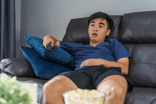 Shocked young man watching at tv and sitting on sofa in the living room