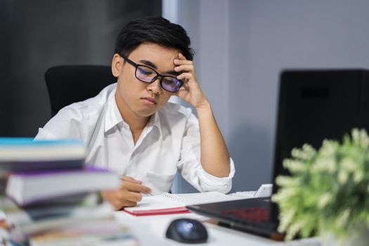 young stressed man studying with book and laptop