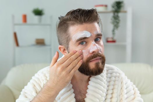 Bearded guy applying anti-wrinkle cream on his face. Skin care and spa for man concept