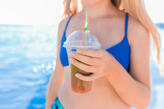 A young girl teenager holds and drink a colored cold non-alcoholic cocktail in her hand against the background of the sea beach.