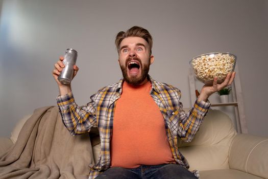 Bearded man watching film or sport games TV eating popcorn in house at night. Cinema, championship and fan.