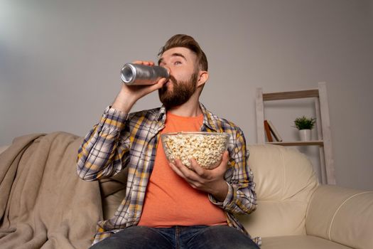 Bearded man watching film or sport games TV eating popcorn in house at night. Cinema, championship and fan.