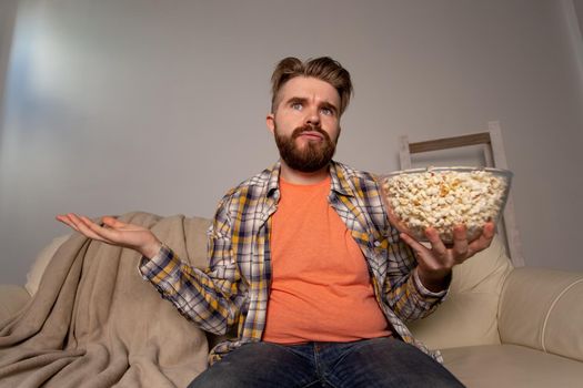 Bearded man watching film or sport games TV eating popcorn in house at night. Cinema, championship and fan.