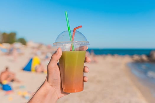 The guy's hand holds a colored chilled non-alcoholic cocktail against the background of the sea beach.